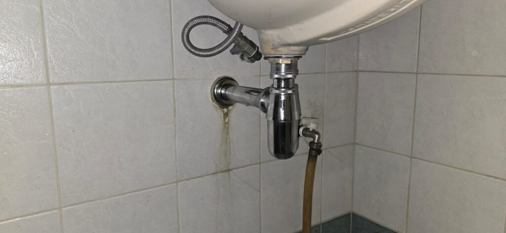 Professional plumber repairing a leaking kitchen sink in a modern Singapore home with a 1-year warranty.